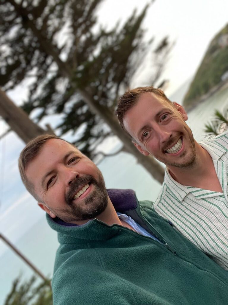 Selfie photo of gay couple tilted at an angle, outside with a tree in the background